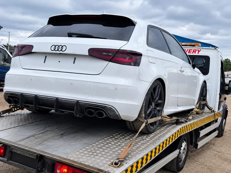 White hatchback secured with wheel straps on a flatbed recovery truck